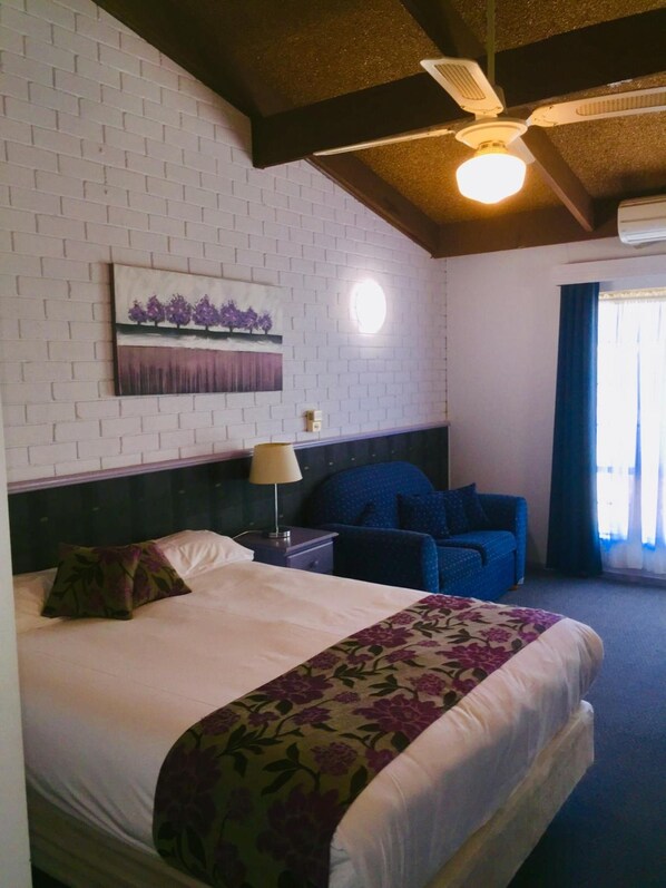Una habitación de hotel con cama, escritorio, silla, ventilador de techo y ventana con cortinas.