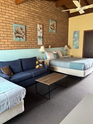 A room with a brick wall, two beds, a sofa, a coffee table, and a ceiling fan.