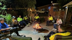 A group of people seated around a fire pit in an outdoor patio area with brick walls and a sign for a guest BBQ. - Bakery Park Motor Inn (Tocumwal)