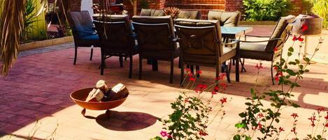 Un patio al aire libre con zona de barbacoa de ladrillo, asientos exteriores y plantas en macetas.