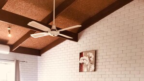 A hotel room with a large bed, a chair, a bedside table with a lamp, a ceiling fan, and a brick-patterned wall. - Bakery Park Motor Inn (Tocumwal)