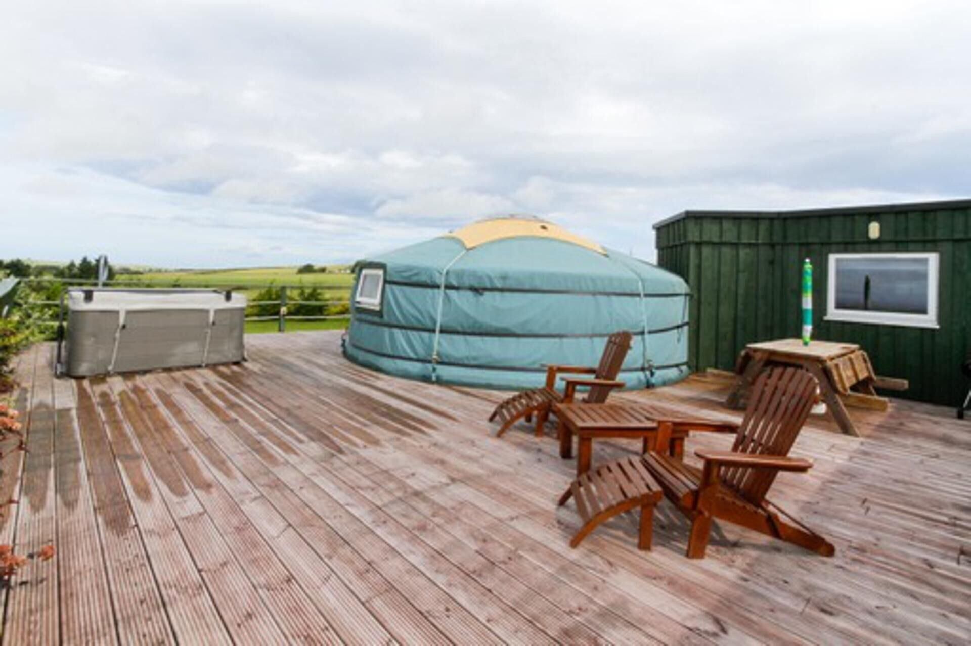 A yurt with a hot tub and wooden deck chairs.
