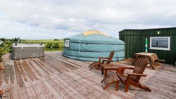 A yurt with a hot tub and wooden deck chairs.