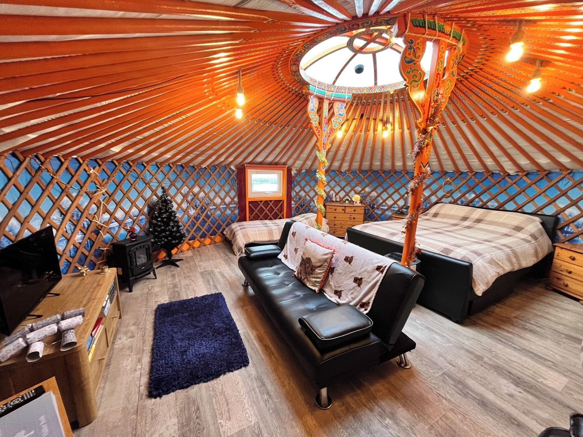 A yurt interior with a bed, sofa, and a small wooden table.