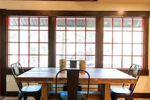 Un comedor con mesa y sillas de madera, ventanas amplias con diseño de cuadrícula y vista a los árboles.