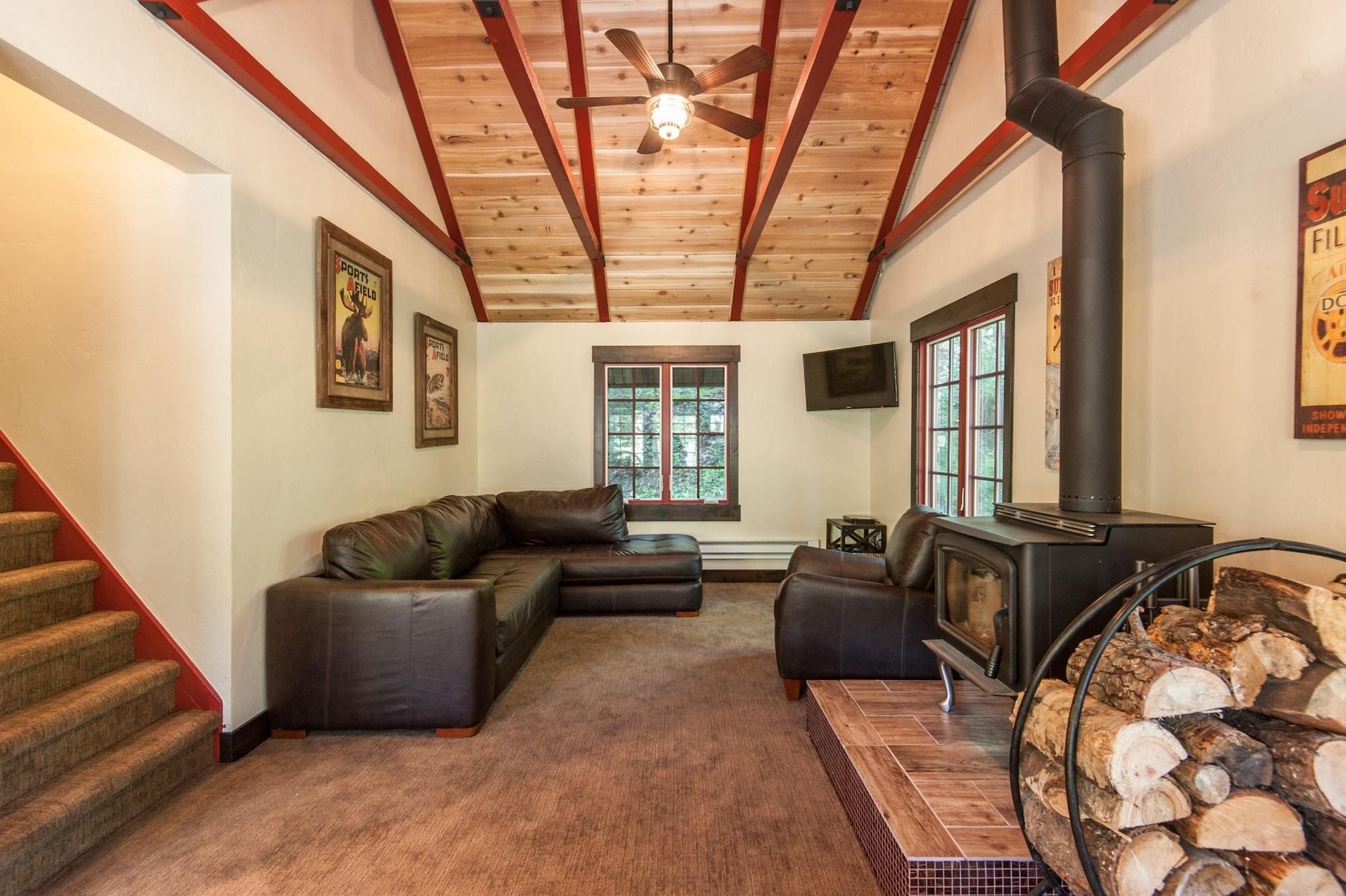 A cozy living room with a fireplace, leather sofas, a TV, and a staircase with red accents.