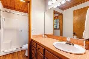 A bathroom with a glass shower enclosure, a white toilet, a wooden vanity with a sink, and a large mirror. - Whiskey Springs By Avantstay Classic Cabin Near (Truckee)