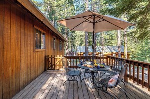 Una terraza de madera con una mesa, sillas y una sombrilla, con vista a un bosque.