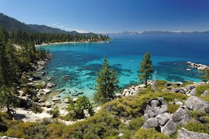 A coastal landscape with clear turquoise waters, rocky shores, and dense green forest.