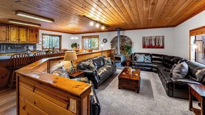 Interior acolhedor de cabana com teto de madeira, lareira de pedra e área de refeições com móveis de madeira.