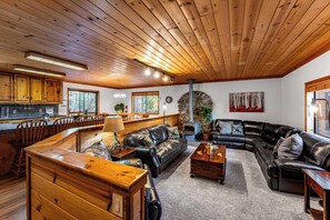 A cozy cabin interior with a wooden ceiling, a stone fireplace, and a dining area with wooden furniture. - Whiskey Springs By Avantstay Classic Cabin Near (Truckee)