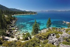 A coastal landscape with clear turquoise waters, rocky shores, and dense green forest. - Whiskey Springs By Avantstay Classic Cabin Near (Truckee)