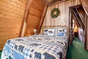 A cozy bedroom with a sloped ceiling, a bed with a checkered blanket, a wall-mounted wreath, and a wooden door. - A Ski View (Big Bear Lake)