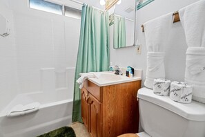 A bathroom with a white sink, wooden cabinet, green shower curtain, white toilet, and a mirror above the sink. - A Ski View (Big Bear Lake)
