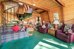 A cozy cabin interior with a plaid sofa, a purple armchair, a fireplace, and a spiral staircase. - A Ski View (Big Bear Lake)
