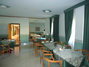 Un comedor con mesas y sillas, una persona al fondo y vista a un pasillo.