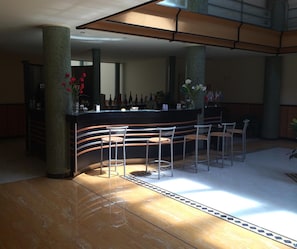 Una zona de bar con una barra curva, varios taburetes y suelo de baldosas.