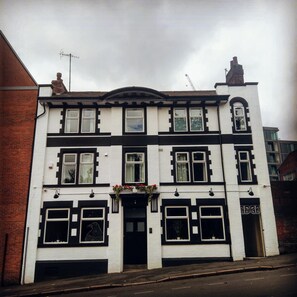 A two-story building with a symmetrical facade, featuring a central entrance with a black door, multiple windows with decorative frames, and a small balcony with flowers. - The Crow Inn (Sheffield)