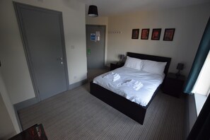 A hotel room with a bed, a nightstand, a door, and a wall with framed pictures. - The Crow Inn (Sheffield)