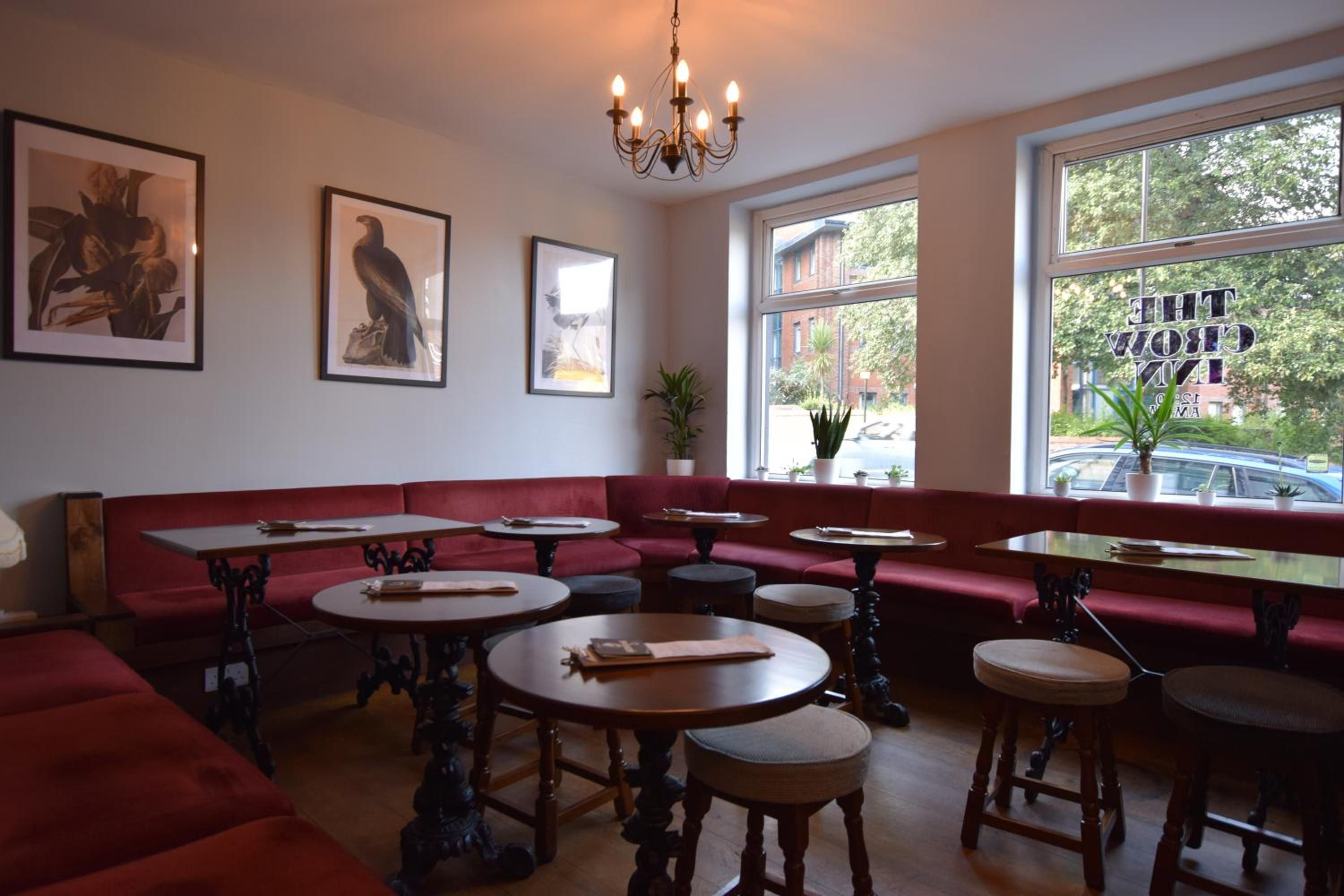 A restaurant interior with a red bench seating area, round tables, and a chandelier.