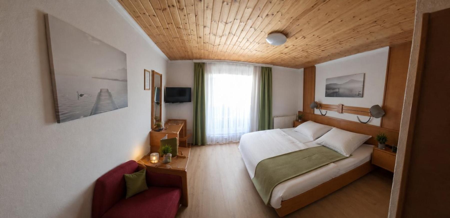 Ein Hotelzimmer mit Bett, Schreibtisch, Stuhl, Fernseher und Bildern an den Wänden.
