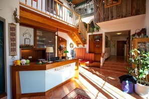 A reception area with a wooden reception desk, a staircase, and a view of the upper floor. - Landhotel Waldmv Hle (Straß im Attergau)