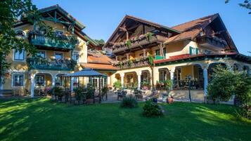 Ein traditionelles Gebäude im europäischen Stil mit mehreren Balkonen, einer überdachten Terrasse und einem gepflegten Garten.