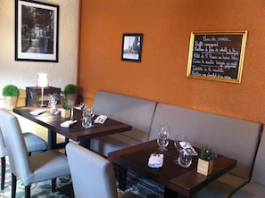 A restaurant with tables set for dining, a menu on the wall, and framed pictures. - Le Brin D Olivier (Bourg-Saint-Andeol)