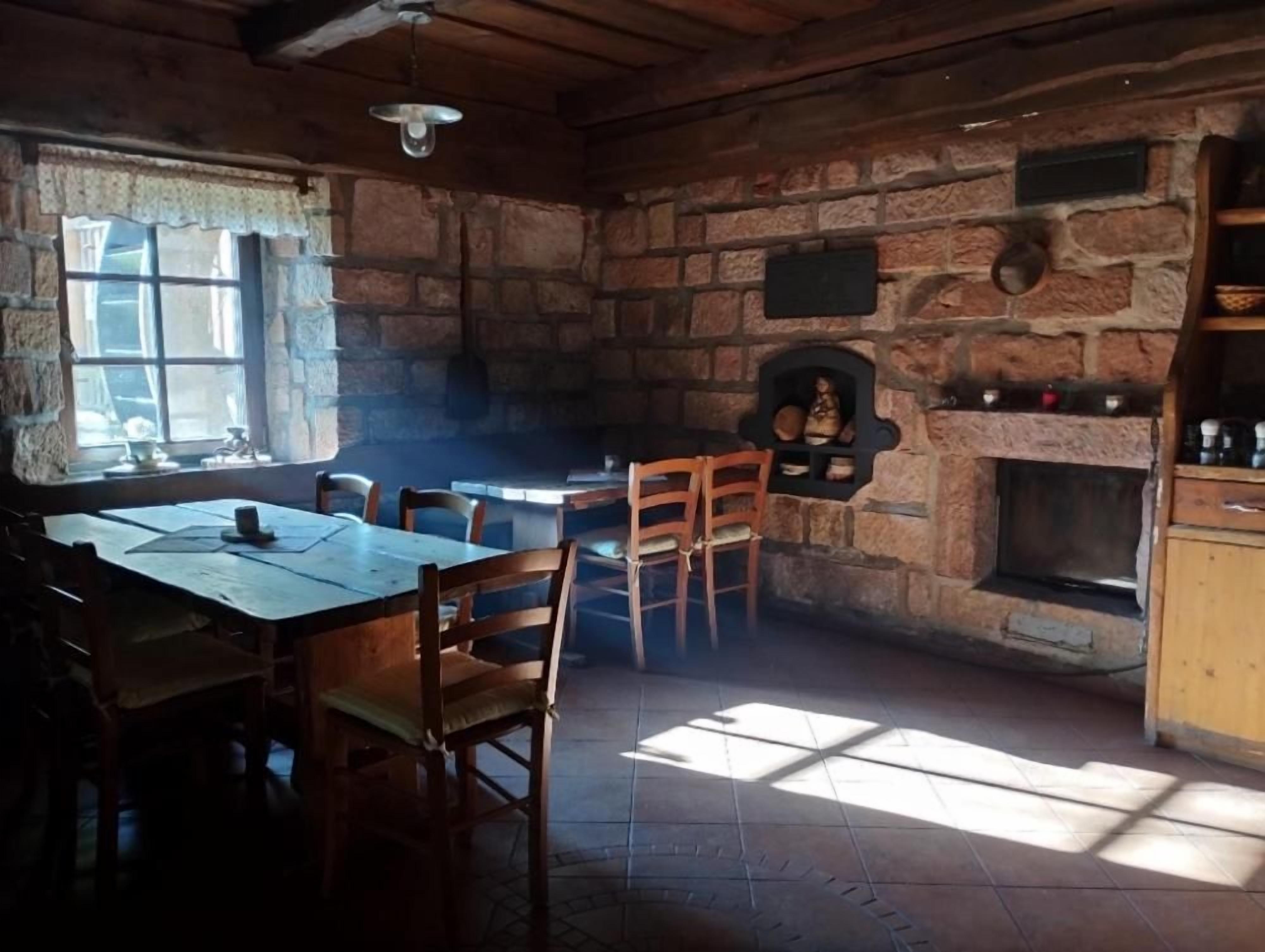 A rustic interior with a stone fireplace, wooden furniture, and a window allowing natural light.