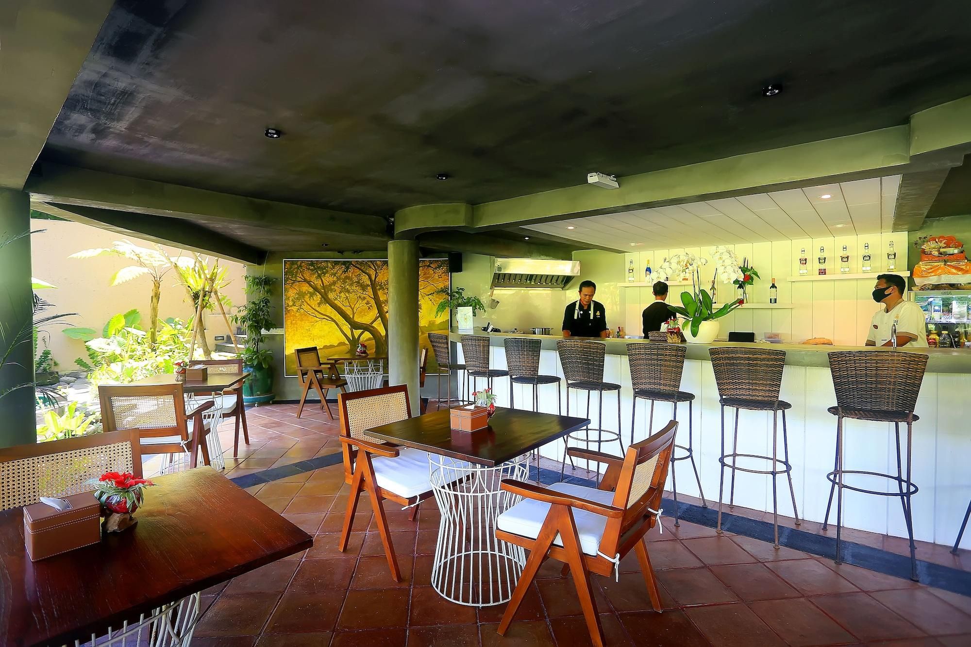 An indoor restaurant with wooden tables and chairs, a bar area, and a kitchen in the background.