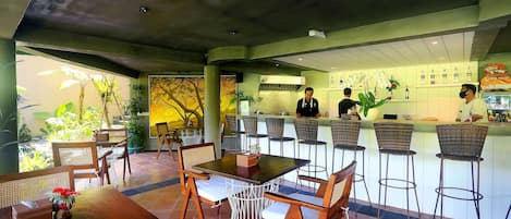 Un restaurante interior con mesas y sillas de madera, una zona de bar y una cocina al fondo.