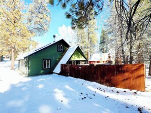 A green house with a snow-covered roof, surrounded by trees and a wooden fence. - Happy On The Lake (Big Bear Lake)