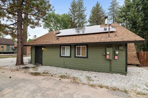 A small, single-story building with a sloped roof, solar panels, and a gravel driveway. - Happy On The Lake (Big Bear Lake)