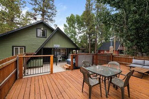 A wooden deck with outdoor furniture, a covered patio area, and a green building with a chimney. - Happy On The Lake (Big Bear Lake)