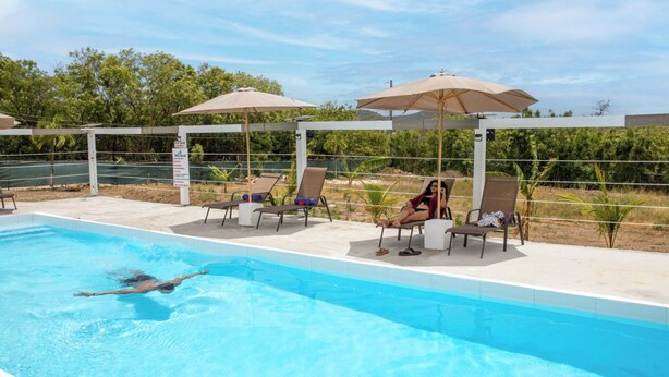 A swimming pool with lounge chairs and umbrellas, surrounded by a fence and greenery. - Neem View Apartments (Falmouth Harbour)