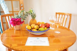 Taula de dinar de fusta amb un plat de fruita, una pinya, un ram de flors i dues copes de vi. Hi ha una targeta de benvinguda sobre la taula.
