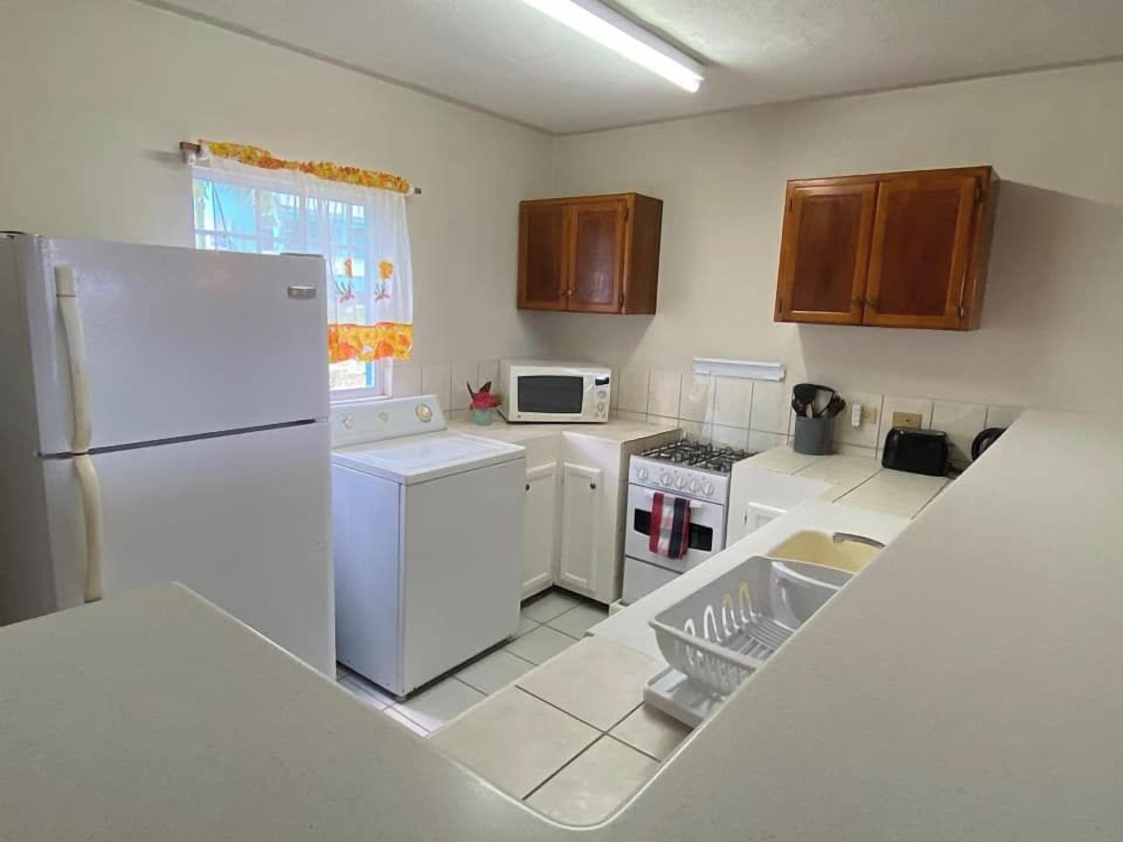 Una cocina compacta con refrigerador, microondas, estufa y gabinetes de madera.