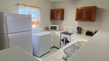 Una cocina compacta con refrigerador, microondas, estufa y gabinetes de madera.