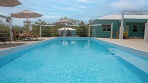 A rectangular swimming pool with clear blue water, surrounded by lounge chairs and umbrellas. - Neem View Apartments (Falmouth Harbour)