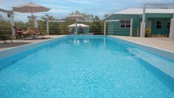 A rectangular swimming pool with clear blue water, surrounded by lounge chairs and umbrellas.