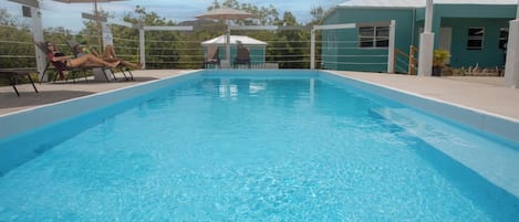 A rectangular swimming pool with clear blue water, surrounded by lounge chairs and umbrellas.