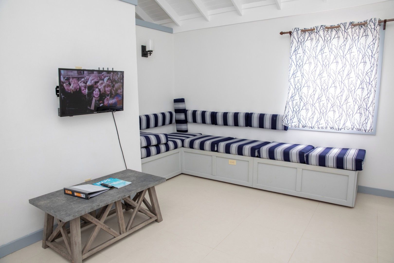 A room with a built-in bench seating, a flat-screen TV mounted on the wall, and a small table with a book.