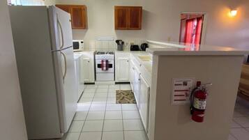 A compact kitchen with white appliances, wooden cabinets, and a fire extinguisher.