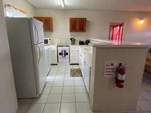 A compact kitchen with white appliances, wooden cabinets, and a fire extinguisher. - Neem View Apartments (Falmouth Harbour)