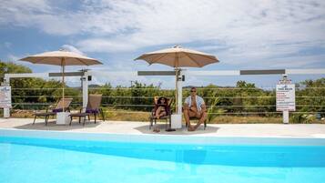 A pool area with lounge chairs, umbrellas, and a sign detailing pool rules.