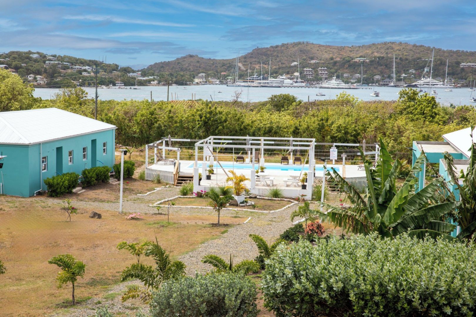 A pool area with a pergola, surrounded by greenery, and a view of boats in the background.