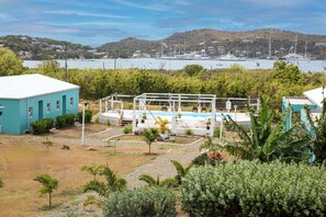 Zona de piscina amb una pèrgola, envoltada de vegetació, i vista a uns vaixells al fons.
