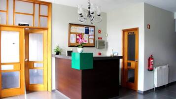 Zona de recepción con un mostrador de madera, un tablón de anuncios y un extintor.