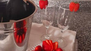 Uma garrafa de champanhe, dois copos e um prato de morangos e chocolate.