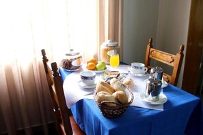 A breakfast table with a blue tablecloth, a basket of bread, a fruit bowl, a coffee pot, and a jar of jam. - Hotel Jorge V (Mirandela)